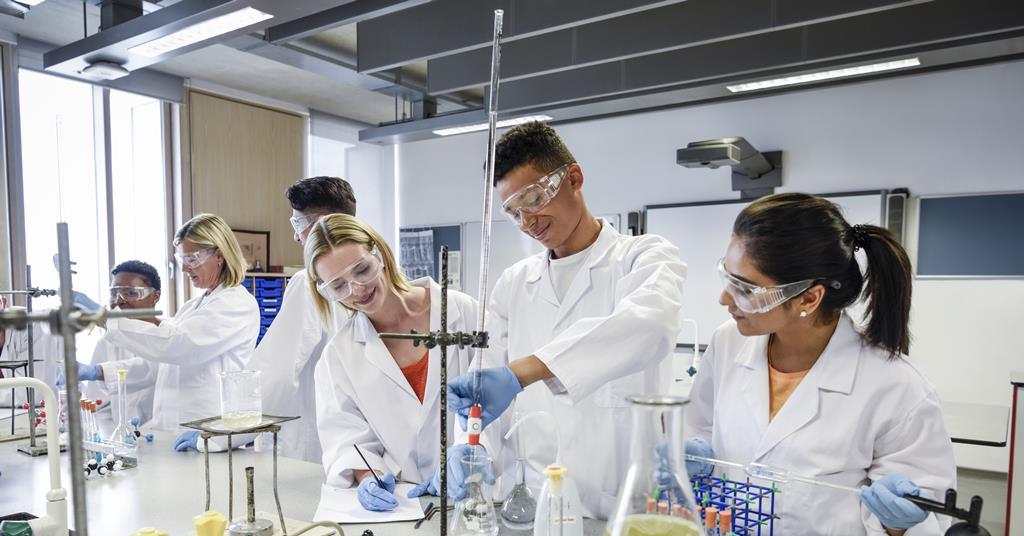 Students wearing lab coats and safety goggles conduct chemistry experiments in a laboratory.