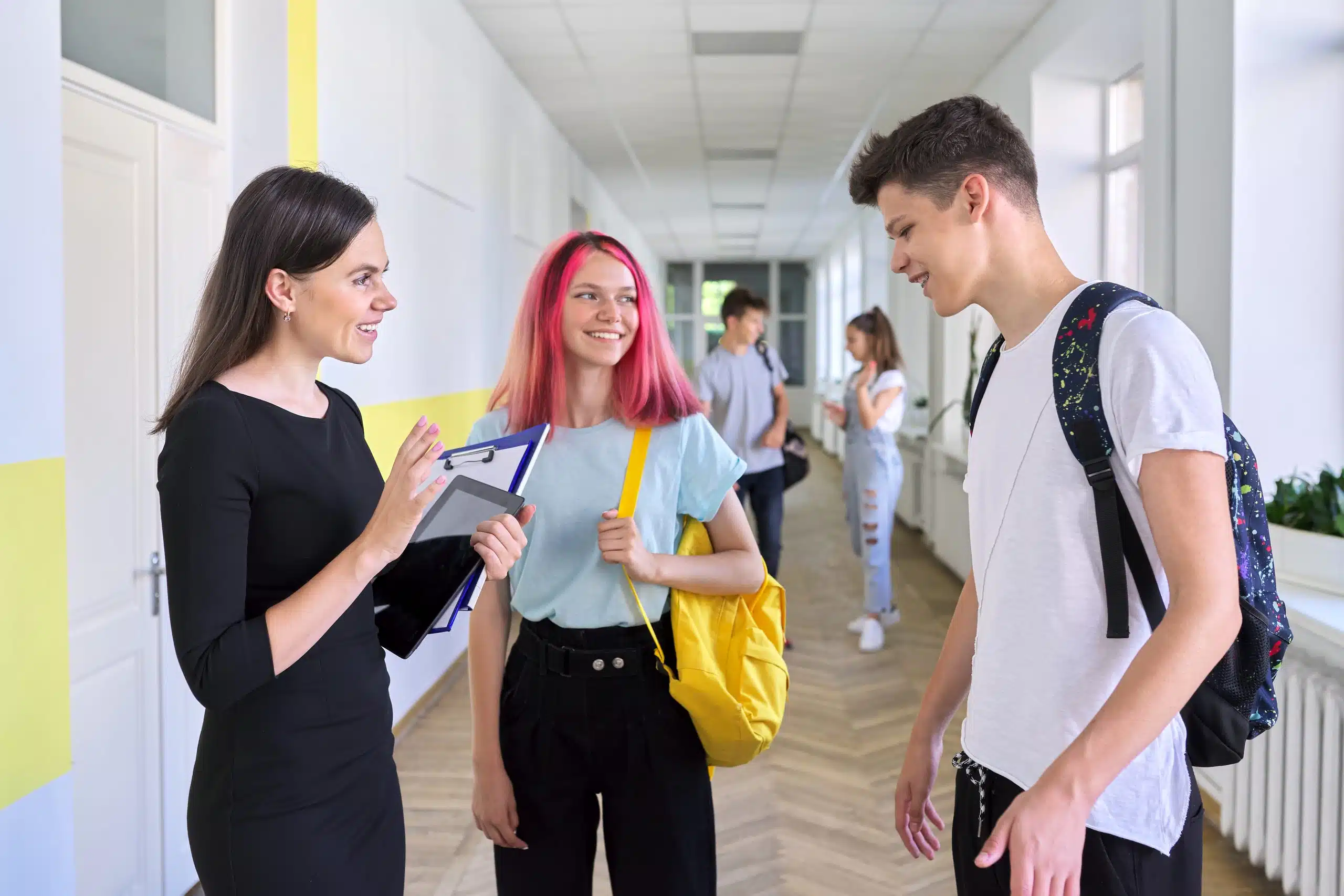 Teenage students talking with a teacher in a school corridor