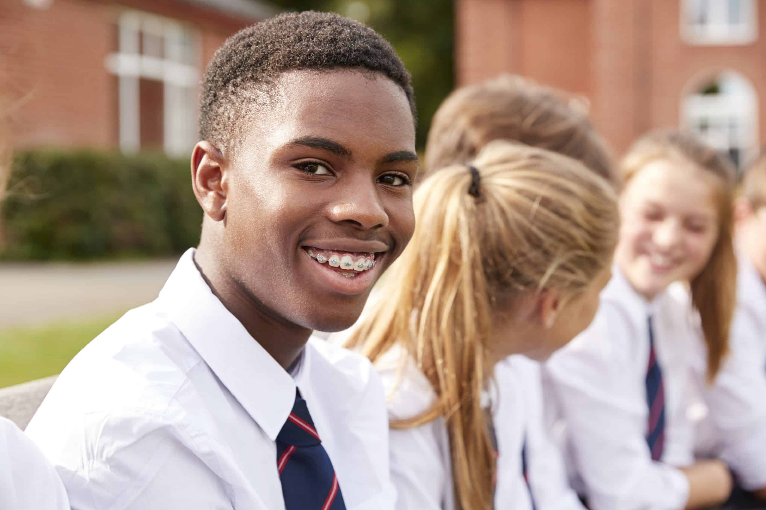 Smiling secondary school student seated outdoors with classmates