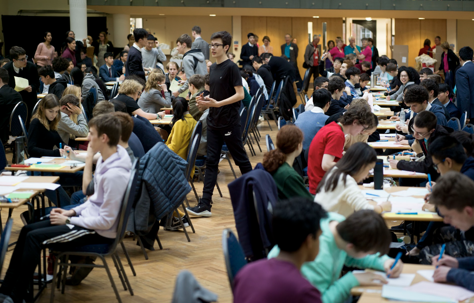 Students working in teams at tables during a large mathematics challenge event