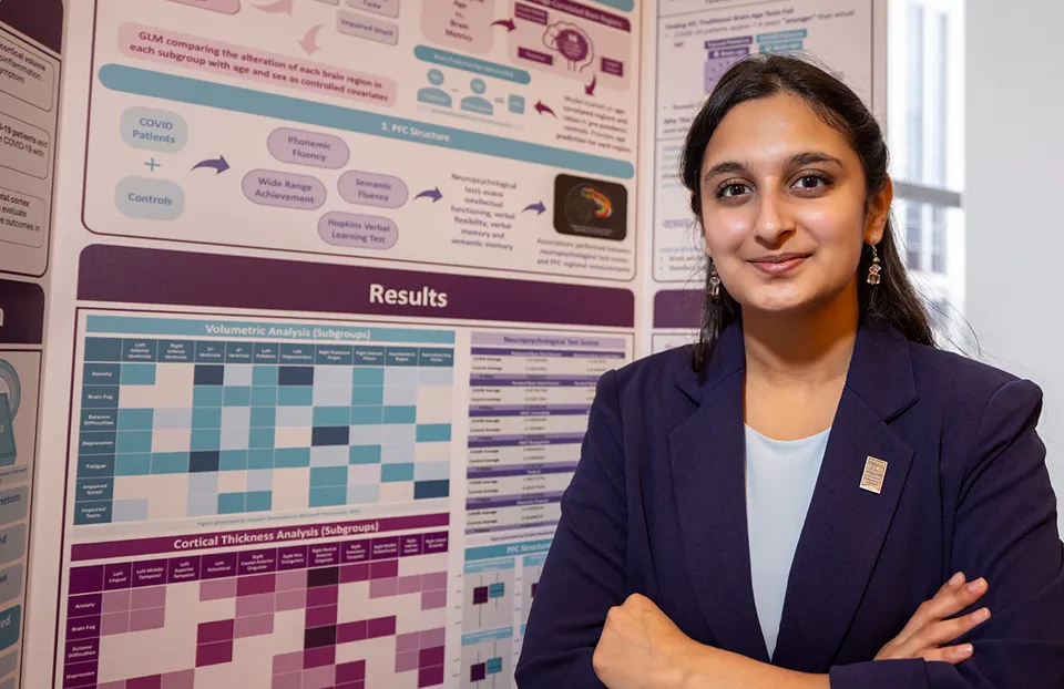 A student researcher standing with folded arms in front of a scientific results poster.