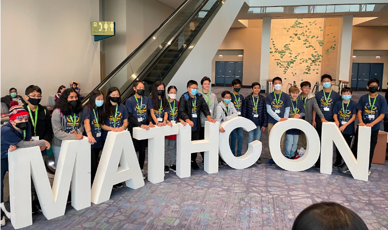 Group of MathCON participants posing behind large white MATHCON letters at an event venue.