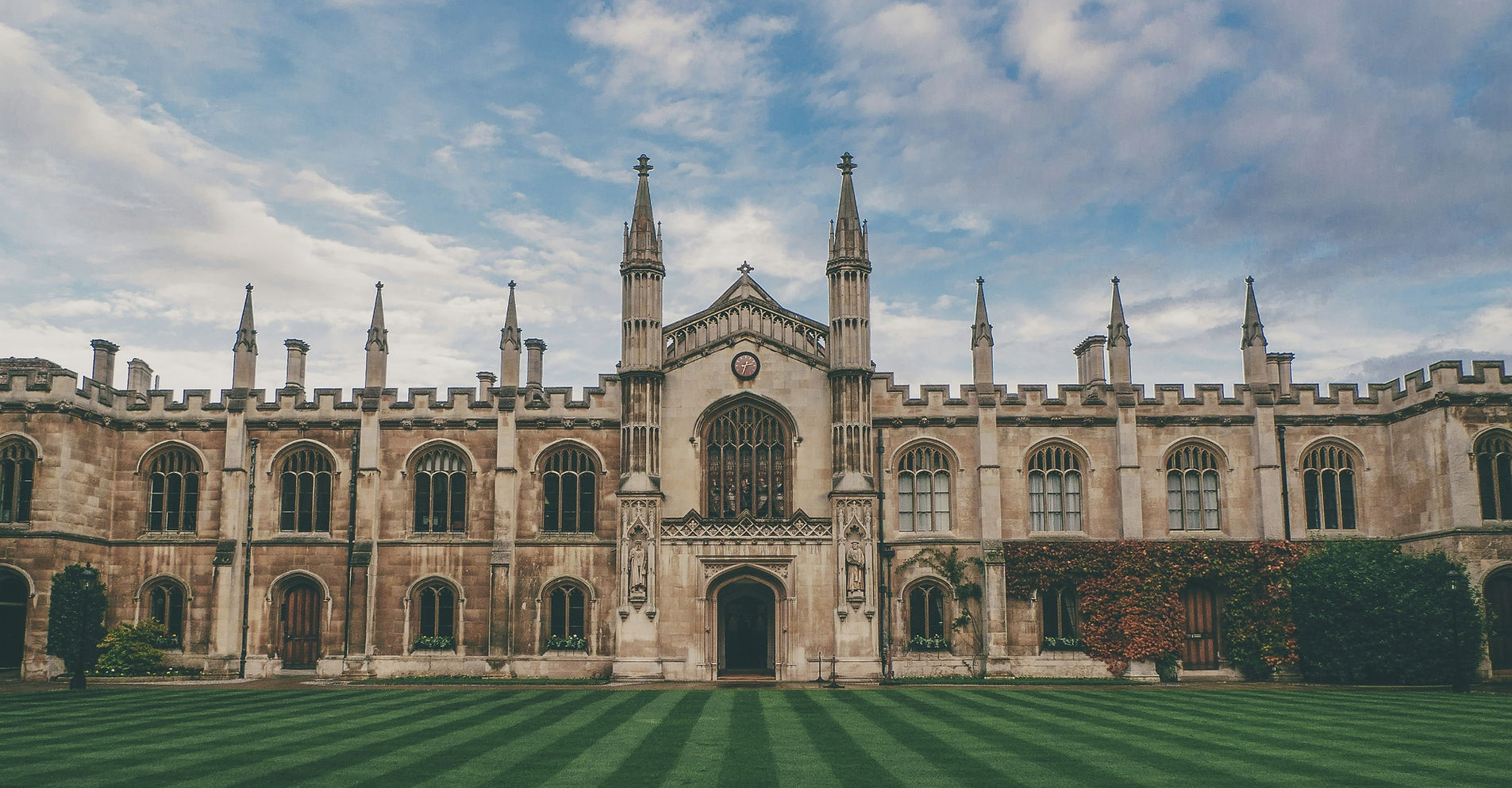 Historic university building and striped lawn beneath a cloudy blue sky