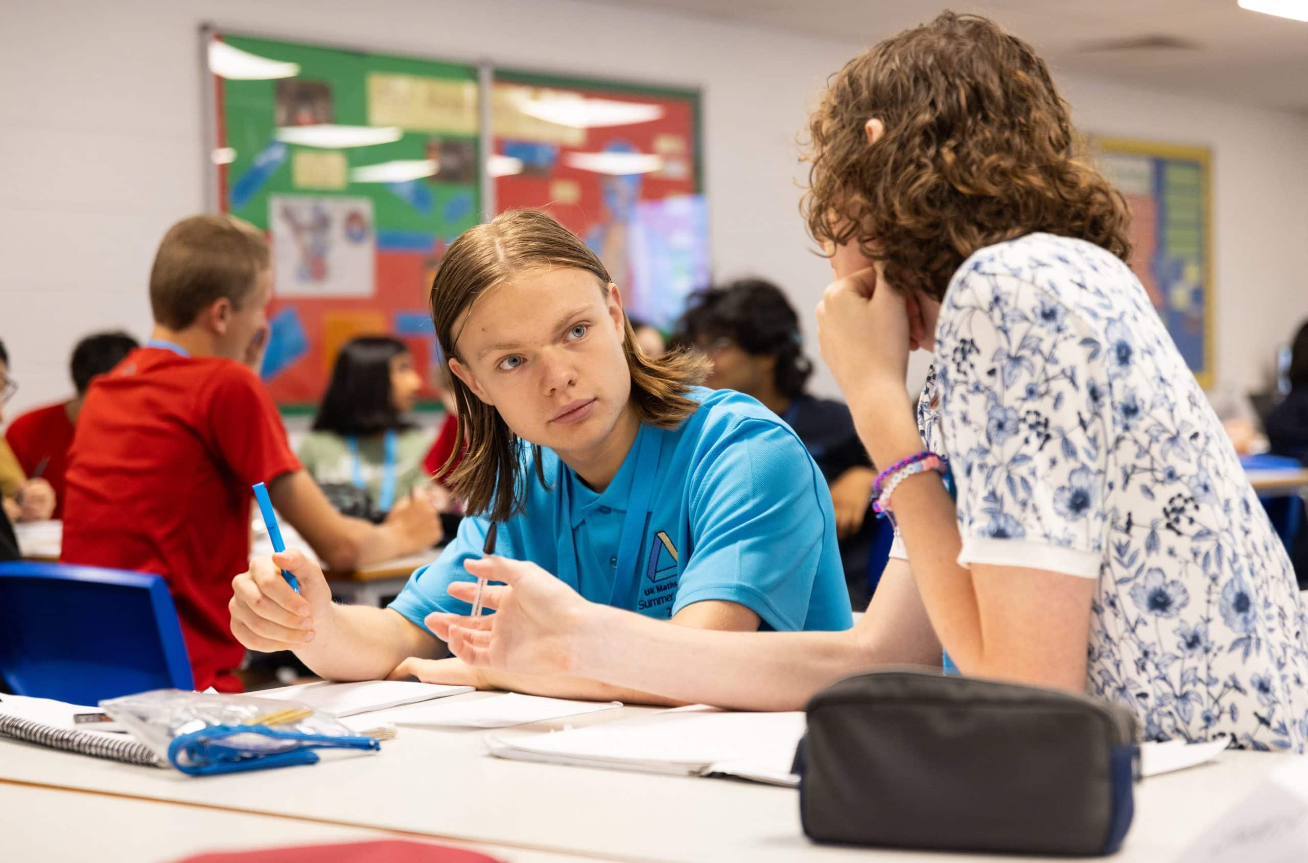 Two students discussing a mathematics problem together in a busy classroom