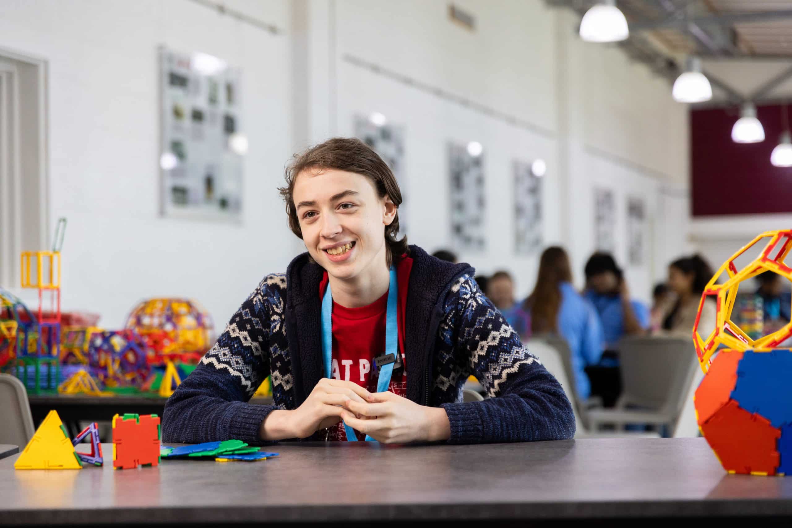 A young person seated at a table with colourful geometric construction models in a mathematics activity space.